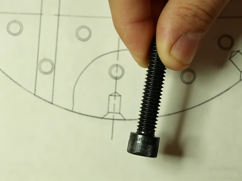 Fastener held over a technical drawing showing hole and countersink detail