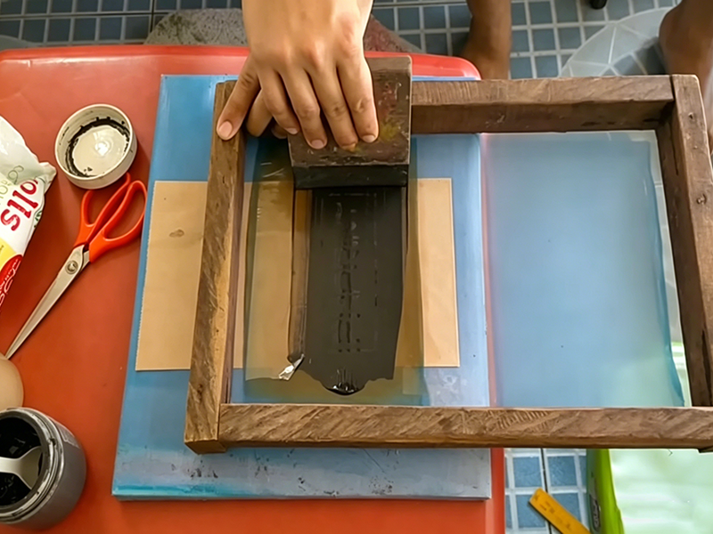 Manual screen printing with squeegee applying black ink through mesh