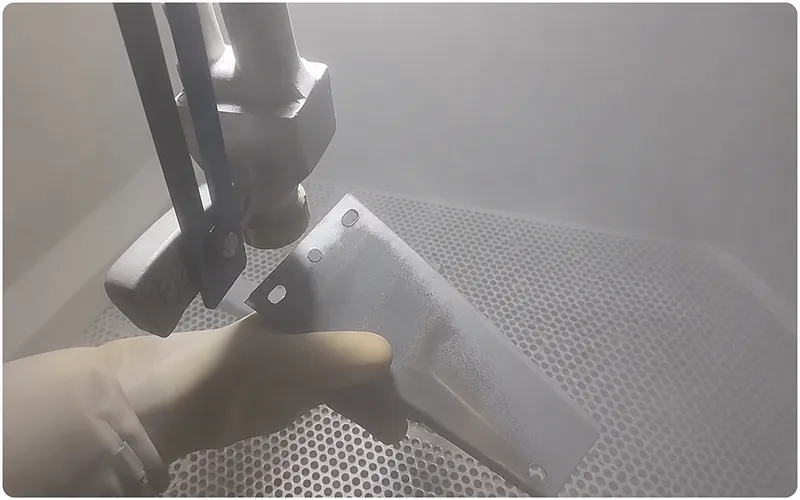Operator bead blasting a metal bracket inside an enclosed blasting cabinet