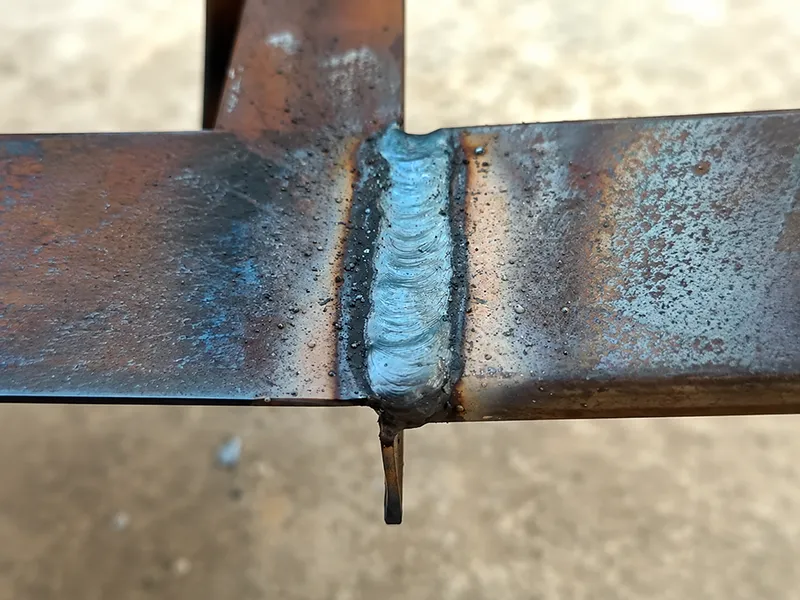 Close-up of a tack weld bead on a steel joint with visible heat marks and weld penetration