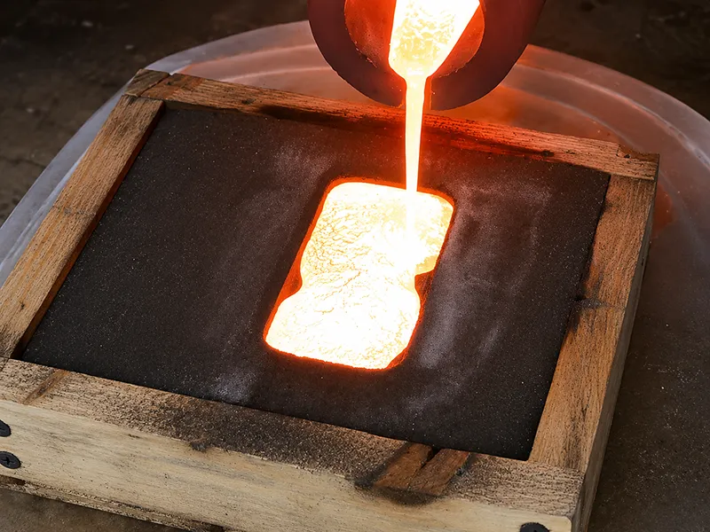 Molten brass being poured into a sand mold during metal casting