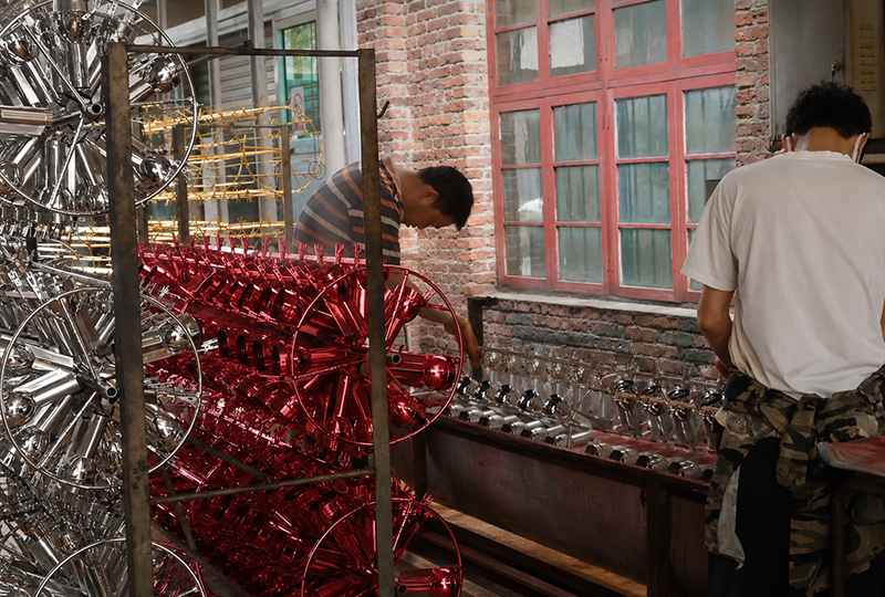 Vacuum Metalizing workshop with red and chrome coated parts on rotating racks