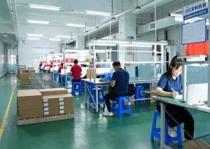Workers checking components and completing paperwork at illuminated factory inspection workstations.