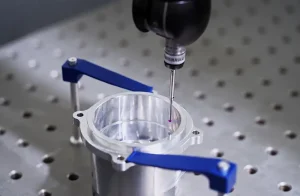 CNC machining inspection using a CMM probe to measure a metal housing secured with blue clamps.