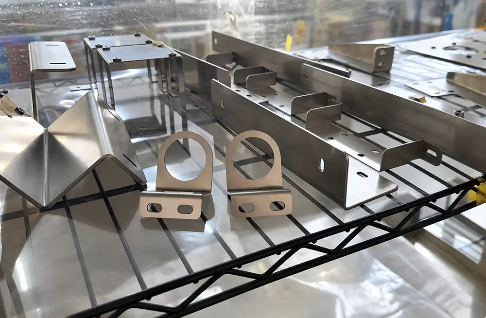 Sheet metal brackets and channels with circular holes and mounting slots arranged on a display shelf.